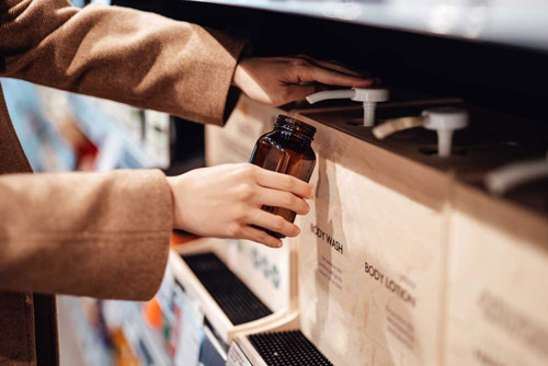 A person filling up a jar with body wash.