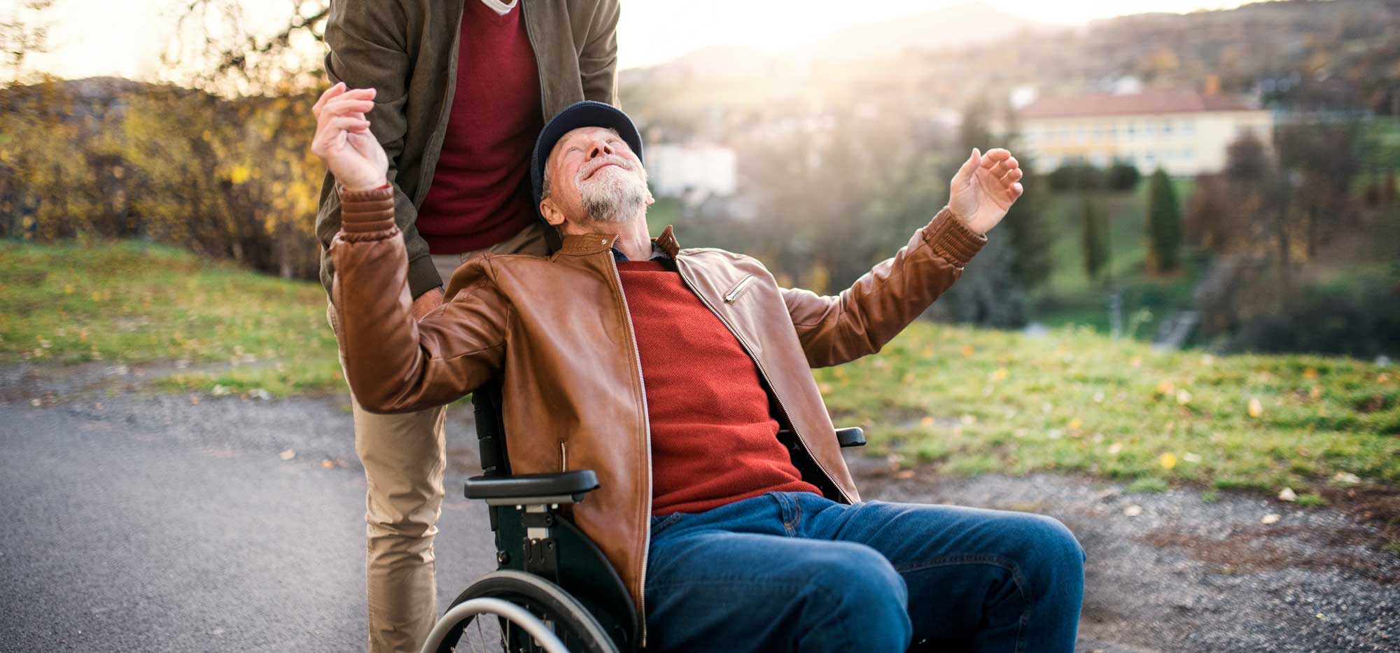 An old man that is being helped by a young man getting around on a wheelchair.